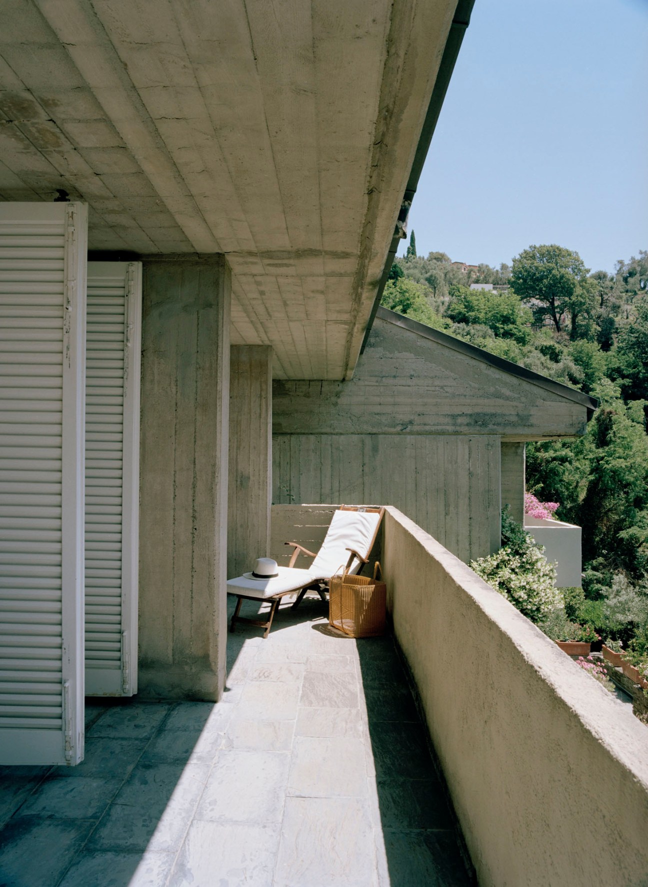 Concrete balcony with white lounge chair and wicker basket overlooking lush green hillside landscape
