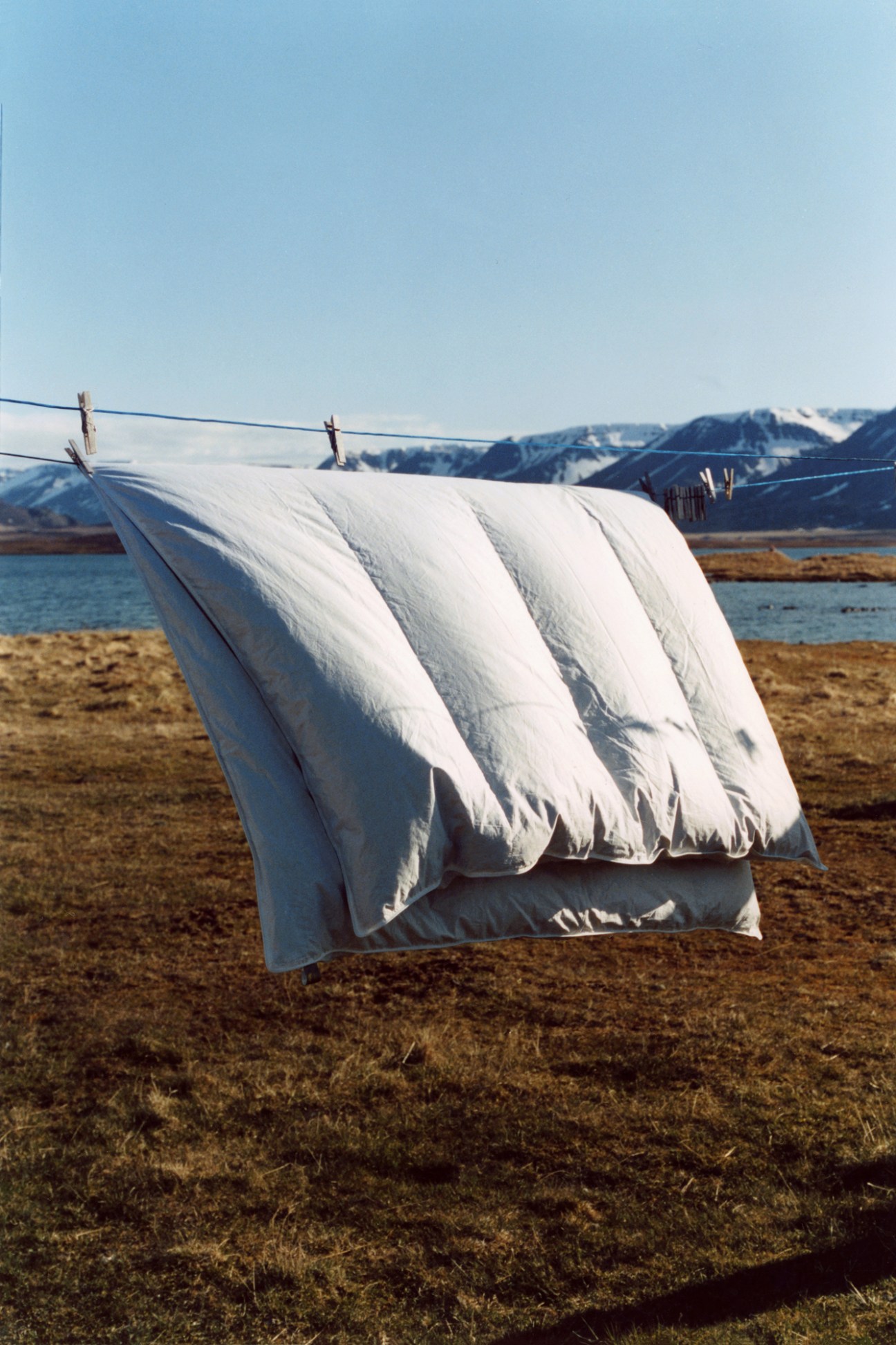 White eiderdown duvet hanging on a clothesline to dry outdoors with mountains and water in the background