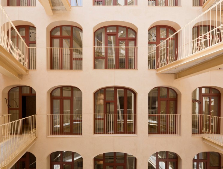 Interior courtyard of La Carbonería building showing multiple levels of arched windows with red frames and white railings