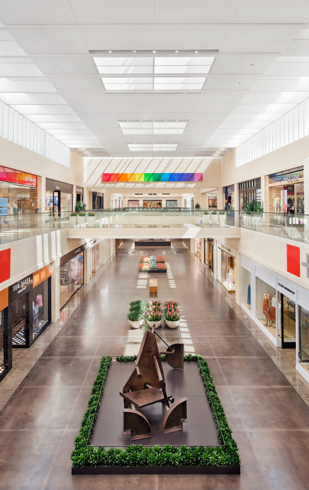 Modern shopping mall interior with two levels, geometric skylights, and a sculptural art installation
