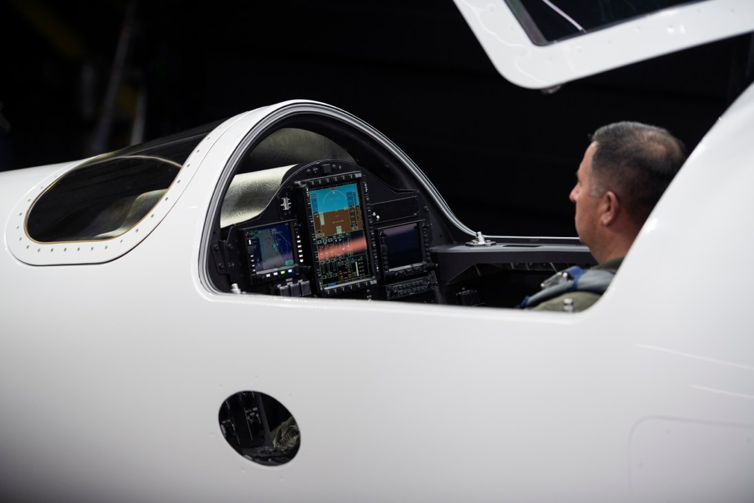Person sitting in aircraft cockpit with digital displays and modern avionics visible