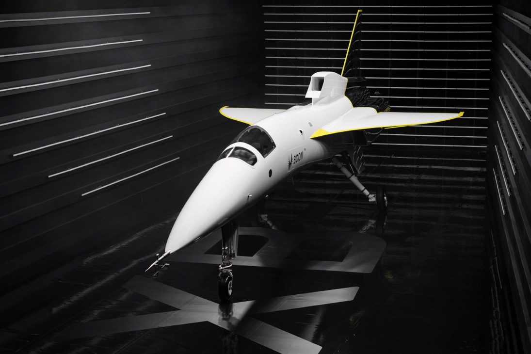White supersonic aircraft with yellow trim displayed in wind tunnel testing facility