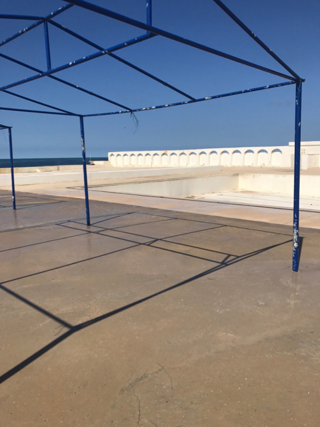 Blue metal frame structure on concrete terrace overlooking sea with white balustrade at Sporting Club Beach