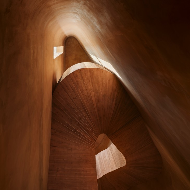Curved brick-lined stairwell with flowing organic architecture and warm lighting
