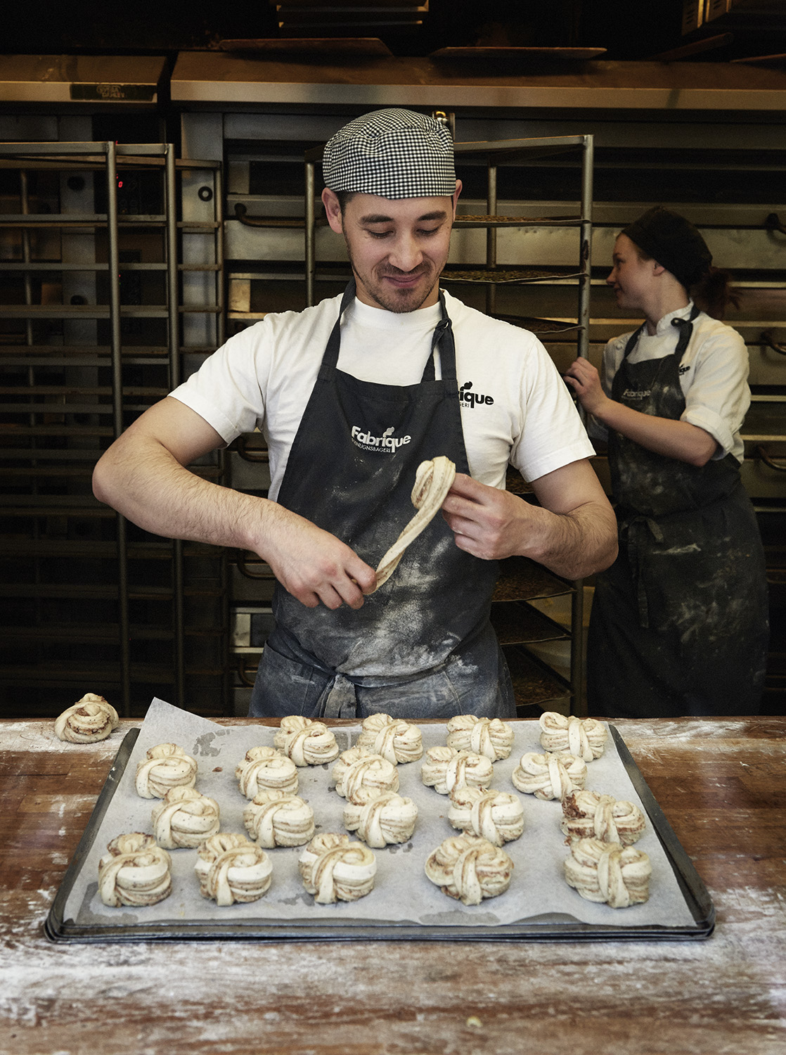 Baker Sherzod Baydadayev shaping dough in Fabrique's kitchen with another baker in background.