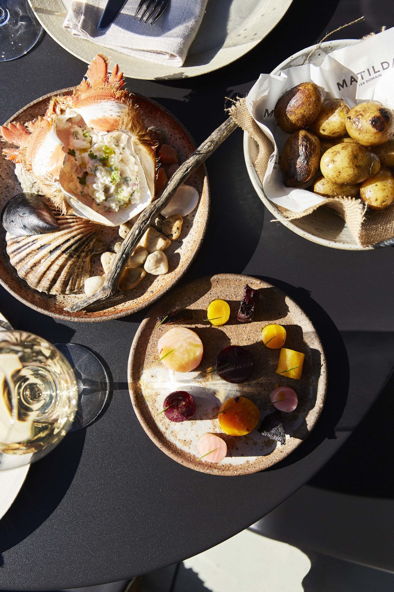 Overhead view of plated seafood dishes at Entrecôte restaurant including oyster, roasted potatoes, and colorful vegetables with wine glass.