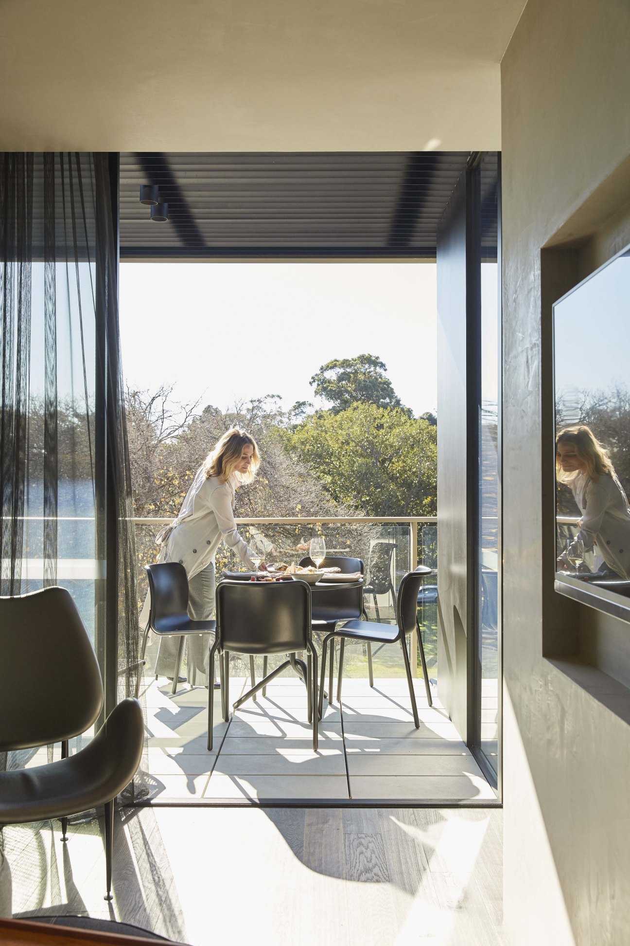 Woman dining on a modern balcony overlooking lush green gardens and trees at United Places hotel.