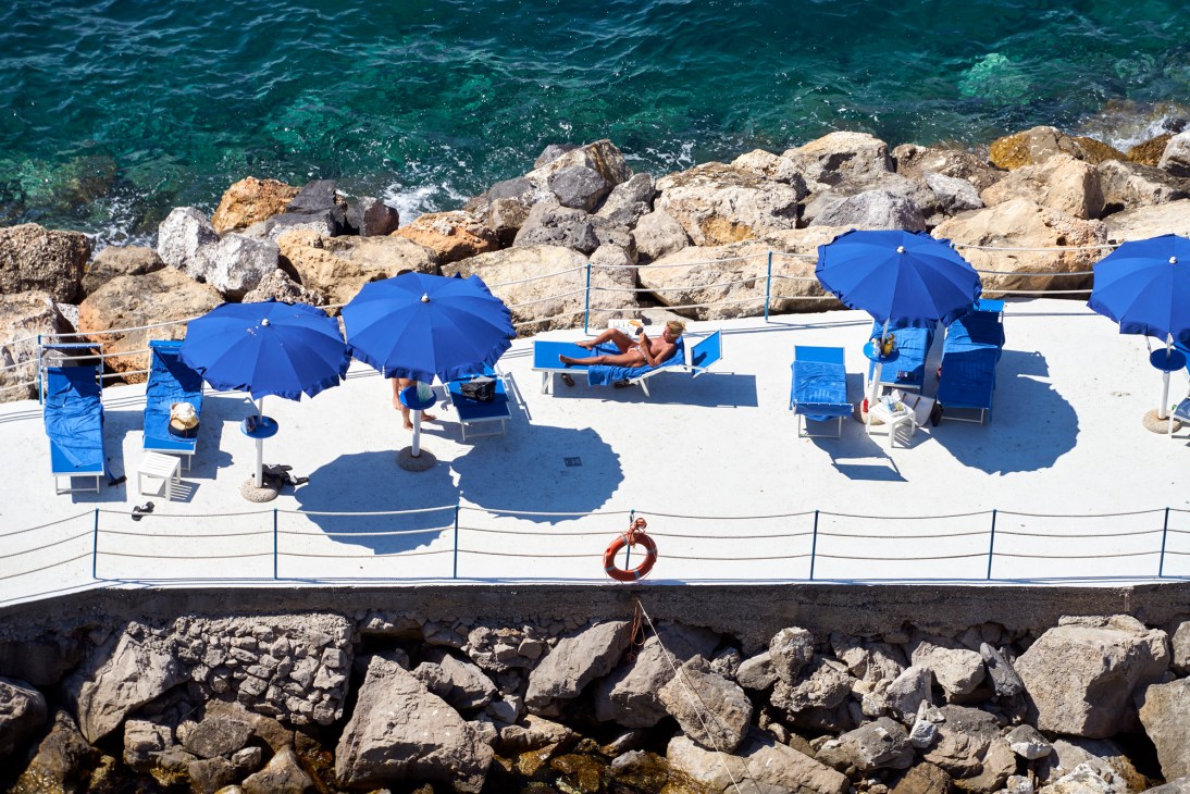 Stylish beach club terrace at Parco dei Principi hotel with blue umbrellas and white loungers overlooking the sea