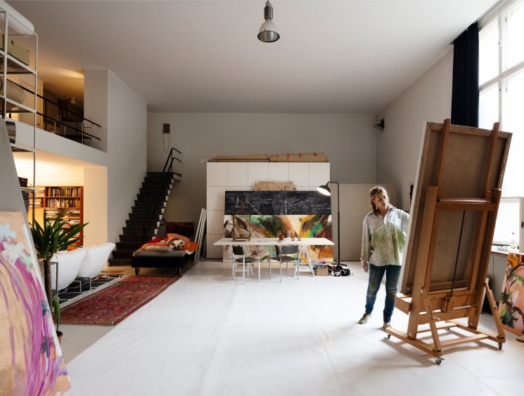 Artist standing in a spacious loft studio surrounded by large canvases.