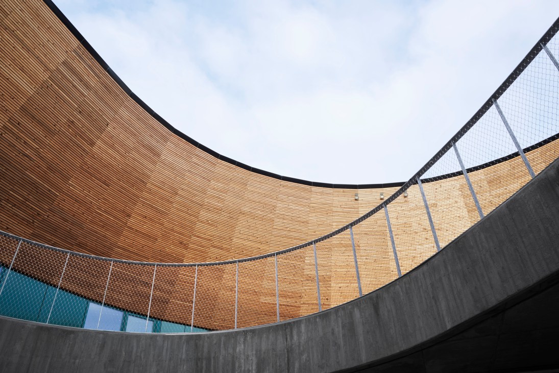 Curved concrete architecture with wooden ceiling and metal mesh safety barrier overlooking circular courtyard