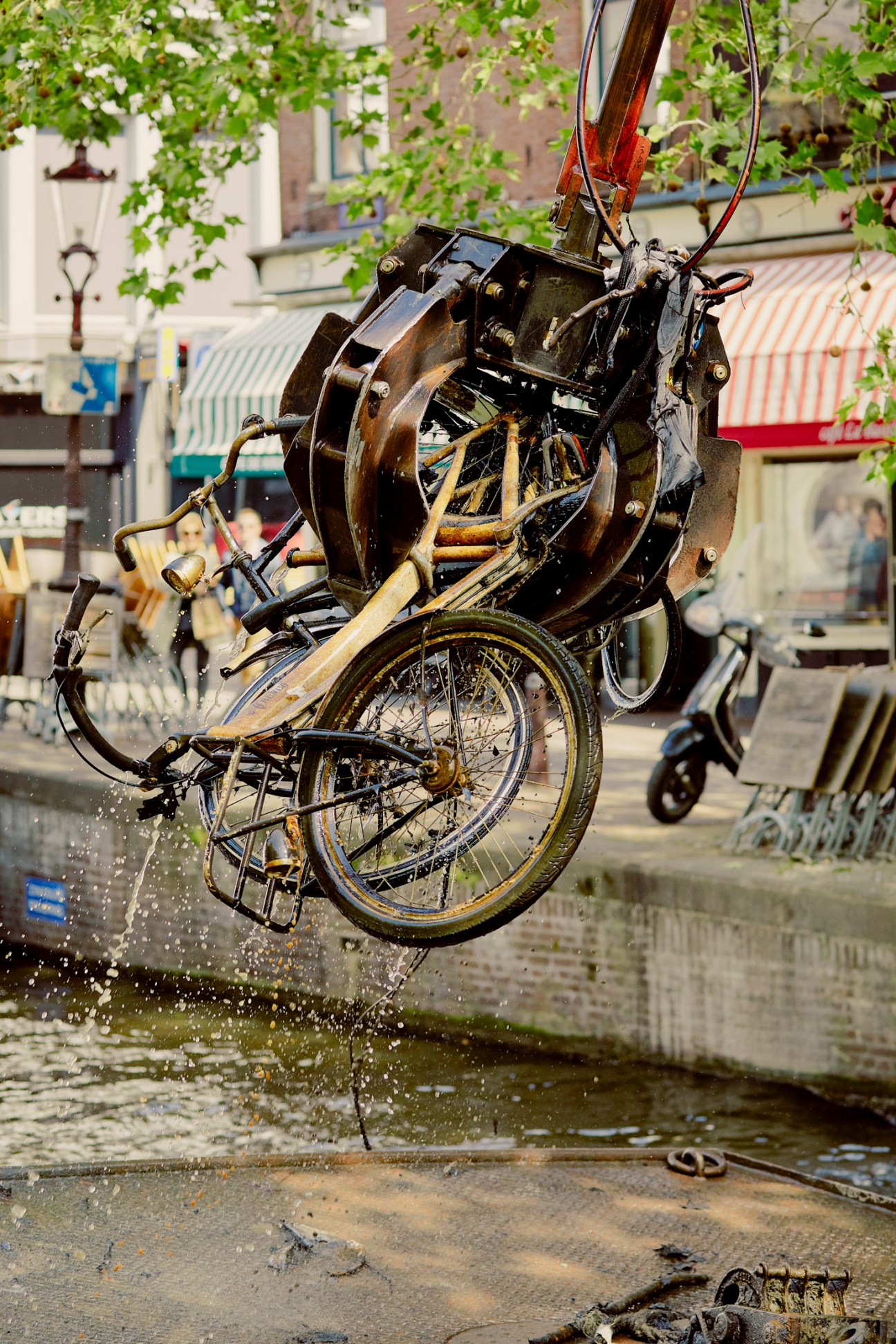 A bicycle being lifted from an Amsterdam canal by a mechanical claw, dripping with water.
