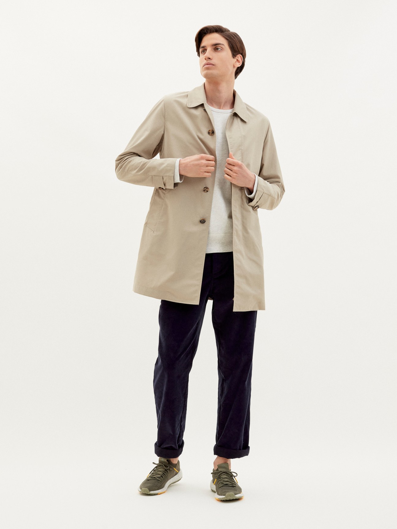 Man wearing beige unlined mac by Valstar x Monocle, white t-shirt, dark trousers and olive trainers.