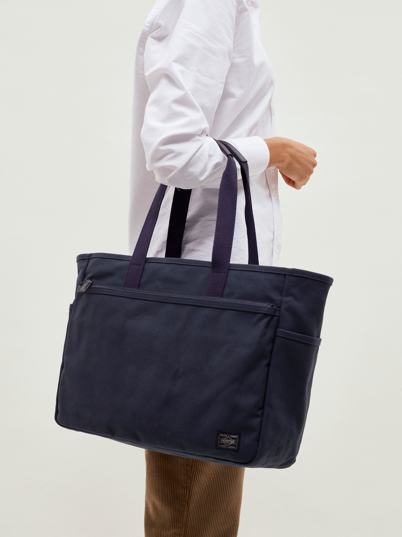 Person in white shirt holding navy canvas Porter x Monocle travel tote bag with shoulder straps