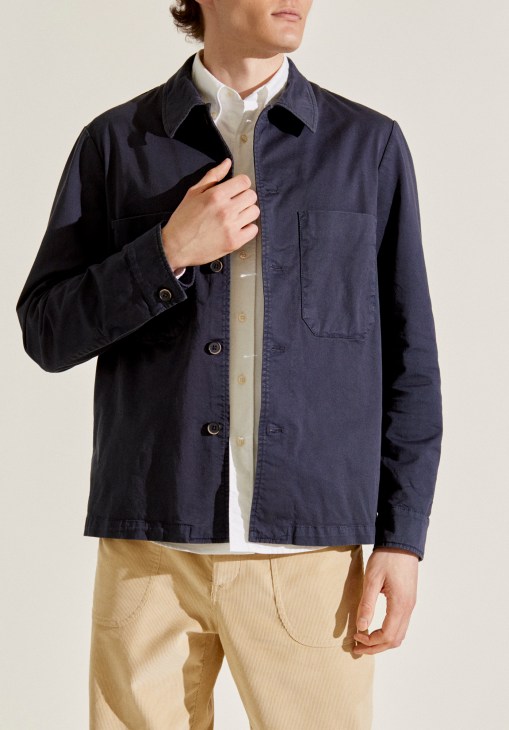 Man wearing navy cotton overshirt by Barena x Monocle over cream shirt and tan trousers.