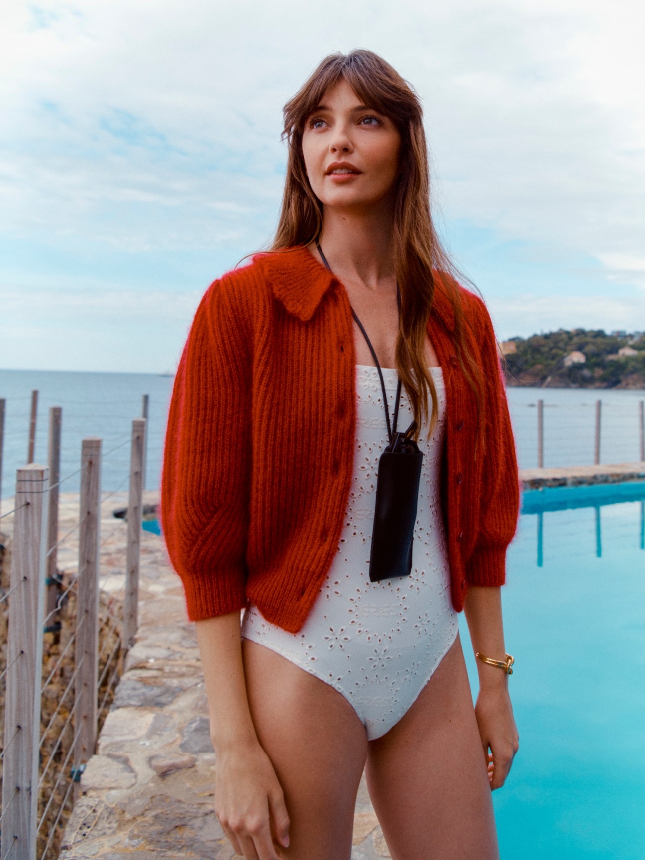 Woman wearing Celine cardigan and swimsuit by Eres at poolside with coastal view.