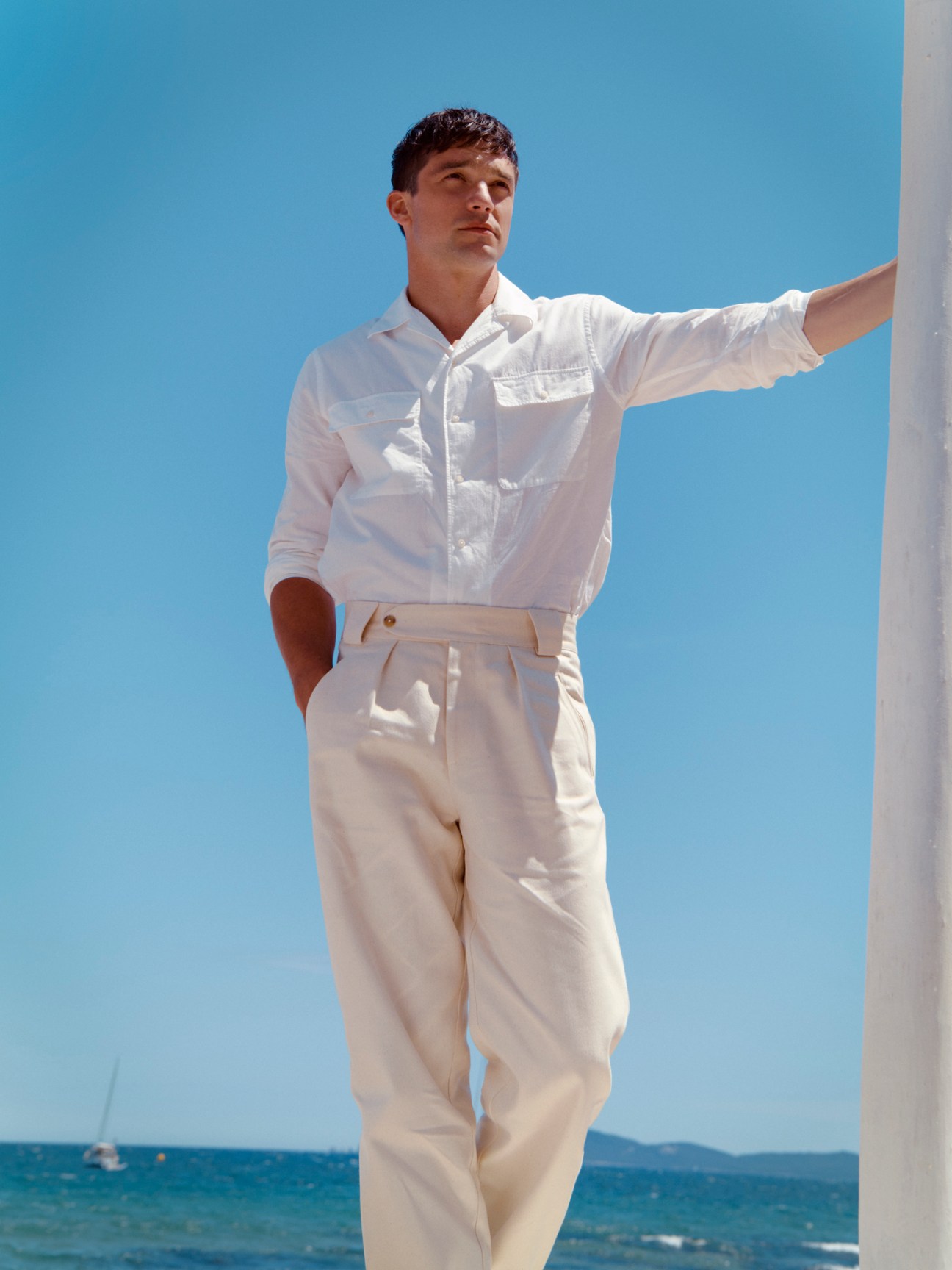 Man in white shirt and cream trousers by De Bonne Facture standing by the sea