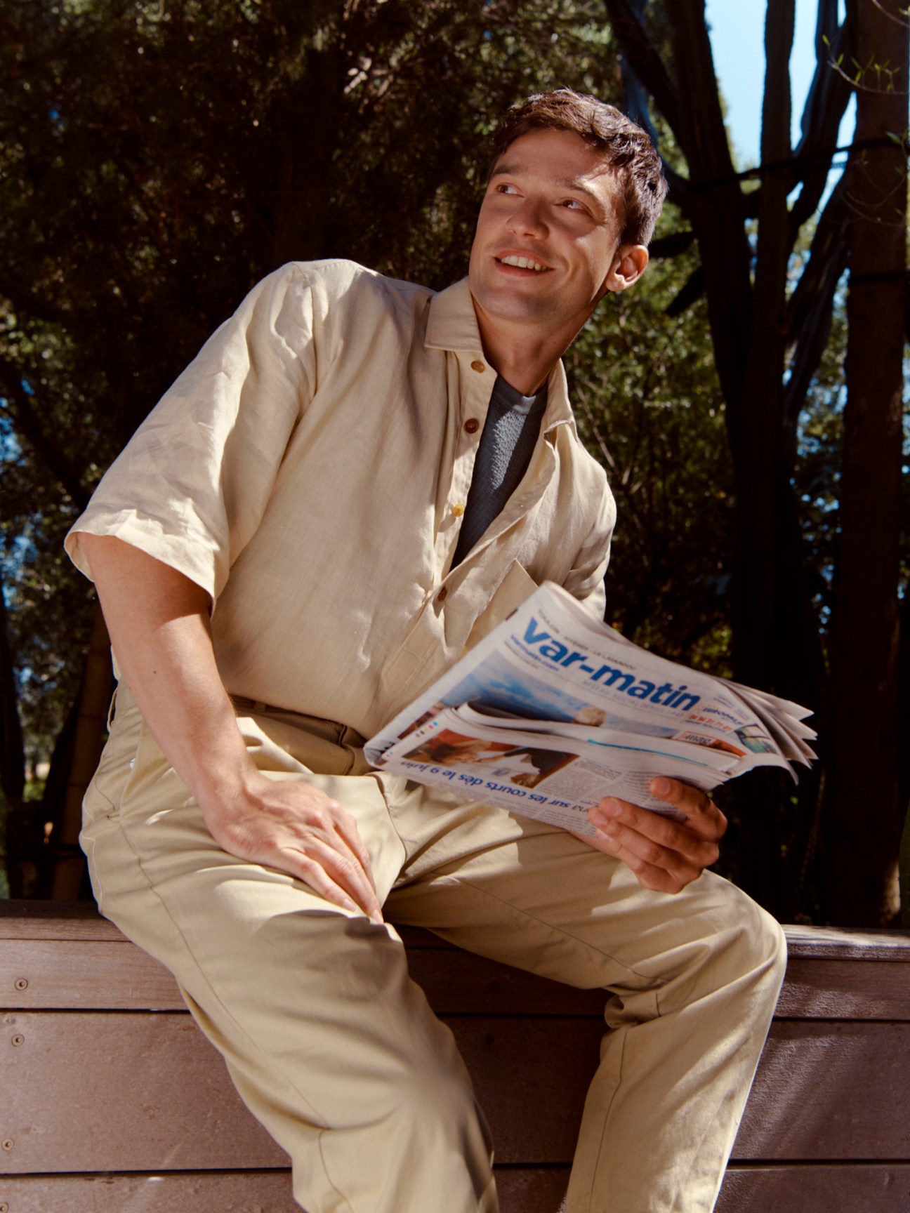 Man in beige Salvatore Piccolo shirt, Brioni t-shirt and Casey Casey trousers sitting on a bench reading a newspaper.