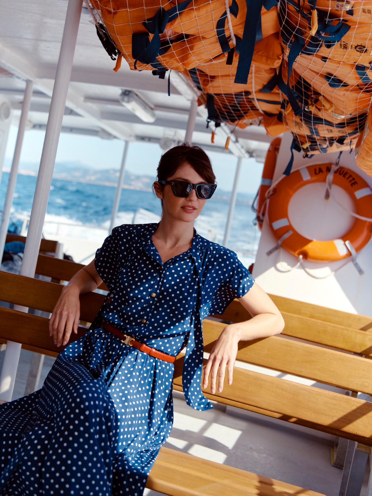 Woman in a blue and white polka-dot Celine dress on a boat, wearing Celine sunglasses and belt.