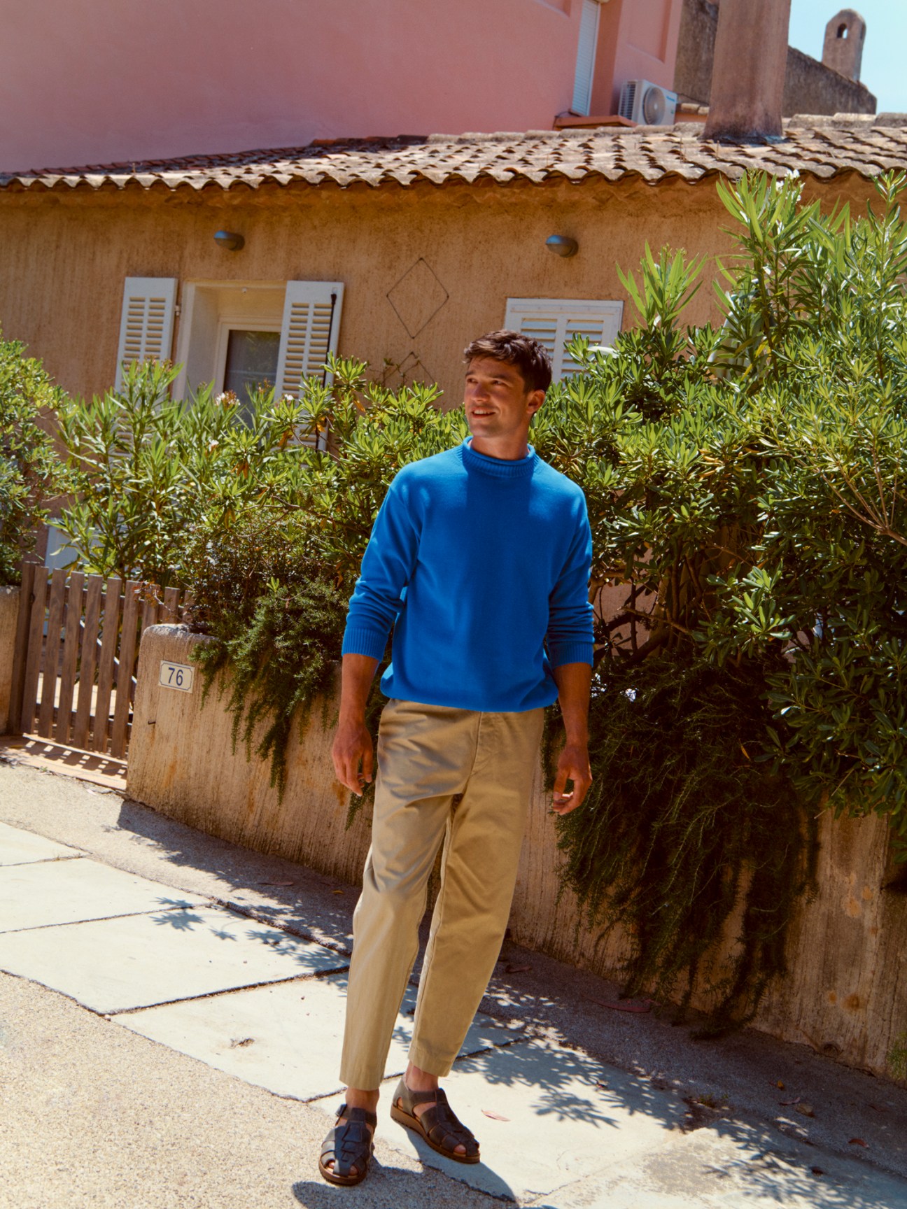 Man wearing blue Arpenteur jumper and Casey Casey trousers standing outside Mediterranean villa.
