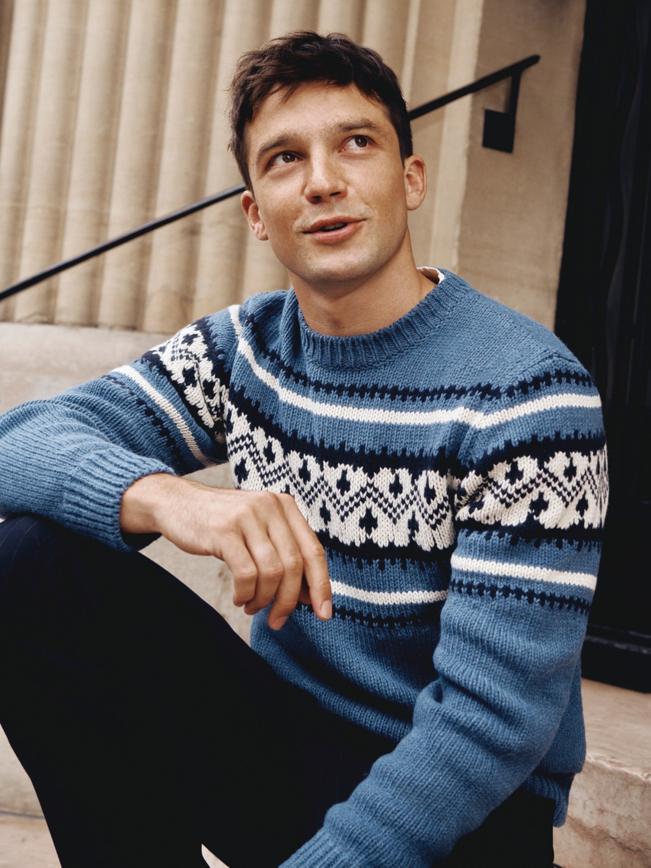 Model wearing blue patterned jumper with geometric Fair Isle design in seated relaxed pose