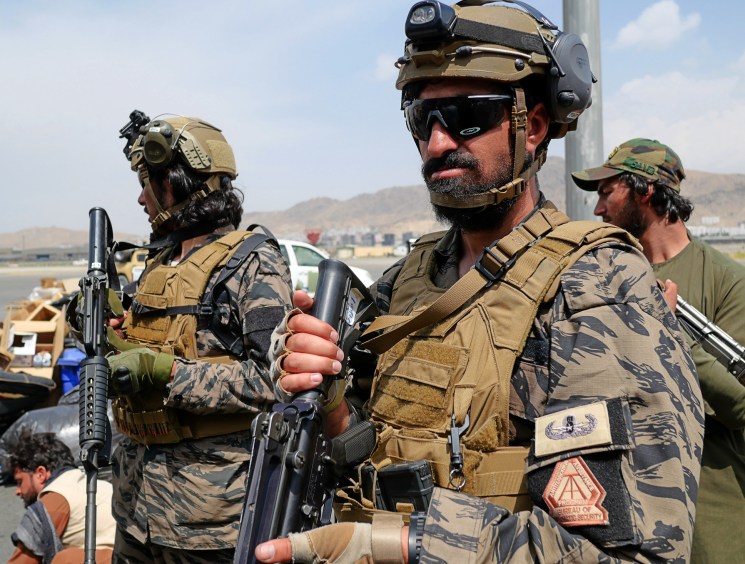 Taliban forces in military fatigues and tactical gear standing with weapons at what appears to be an airport
