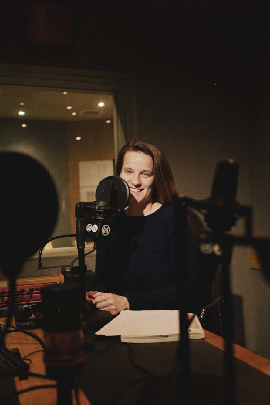 Woman smiling while speaking into a professional microphone in a radio studio