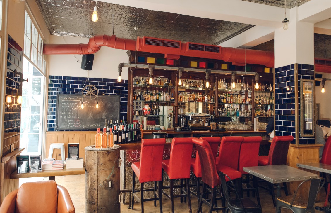 Interior of Aaliya's Books showing restored bar area with red chairs, blue tile walls, and fully stocked shelves