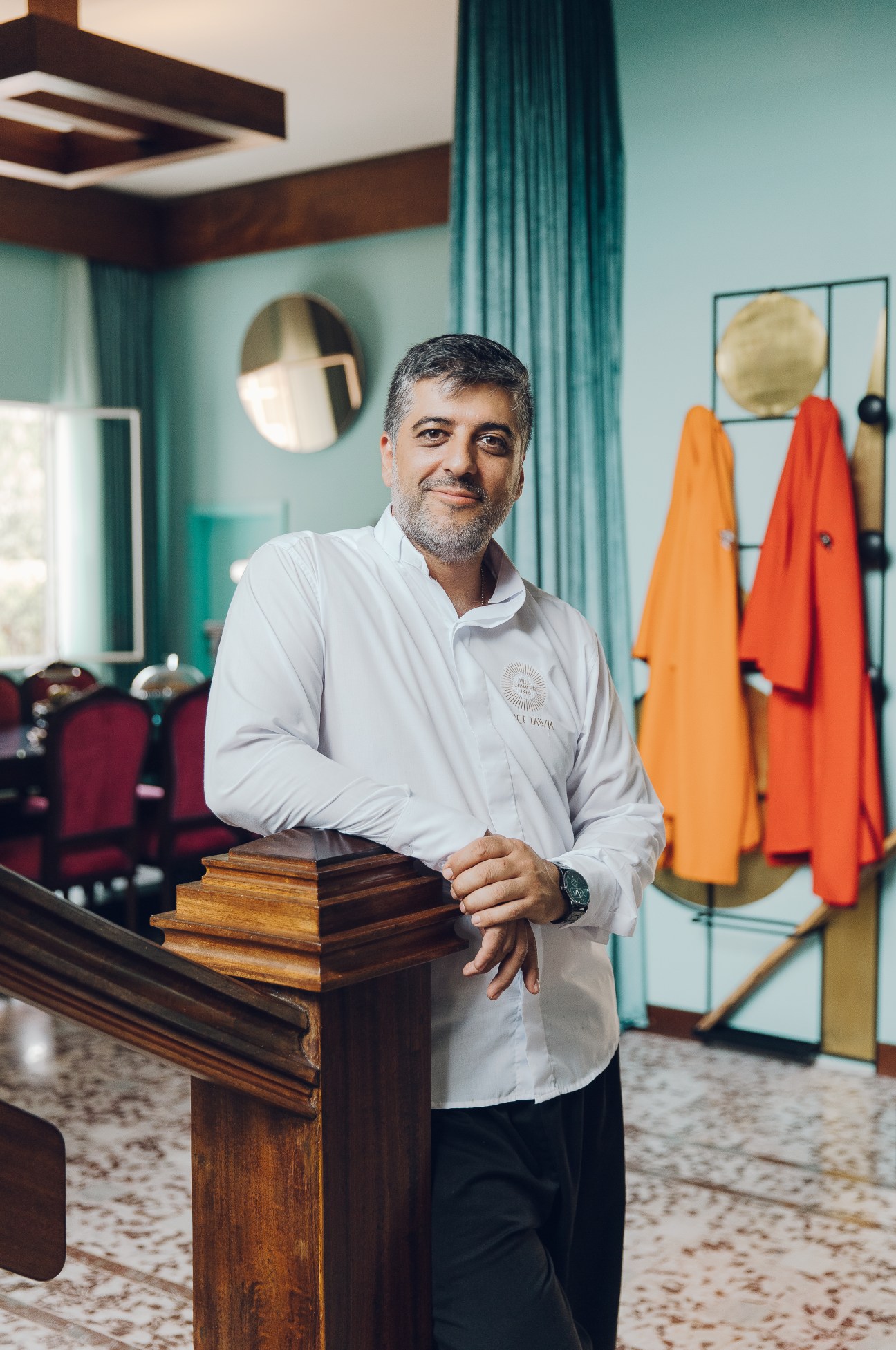 Chef Joseph Tawk stands in a turquoise salon with mid-century modern decor and colorful clothing displays.