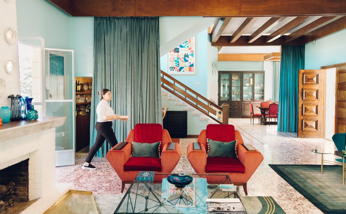 Retro-styled salon with turquoise walls, orange and red mid-century chairs, and wooden beams at Villa Chamoun hotel.
