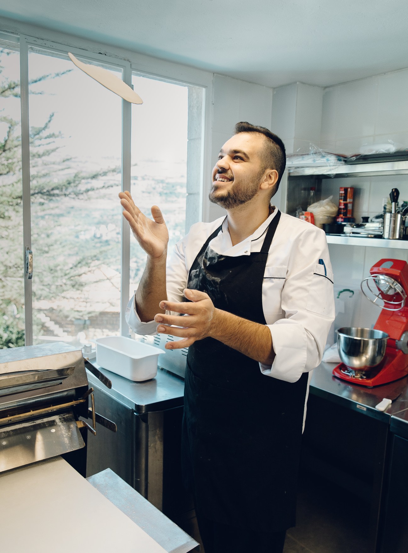 Chef Cool Elie in the kitchen preparing dough, wearing a black apron and white shirt.