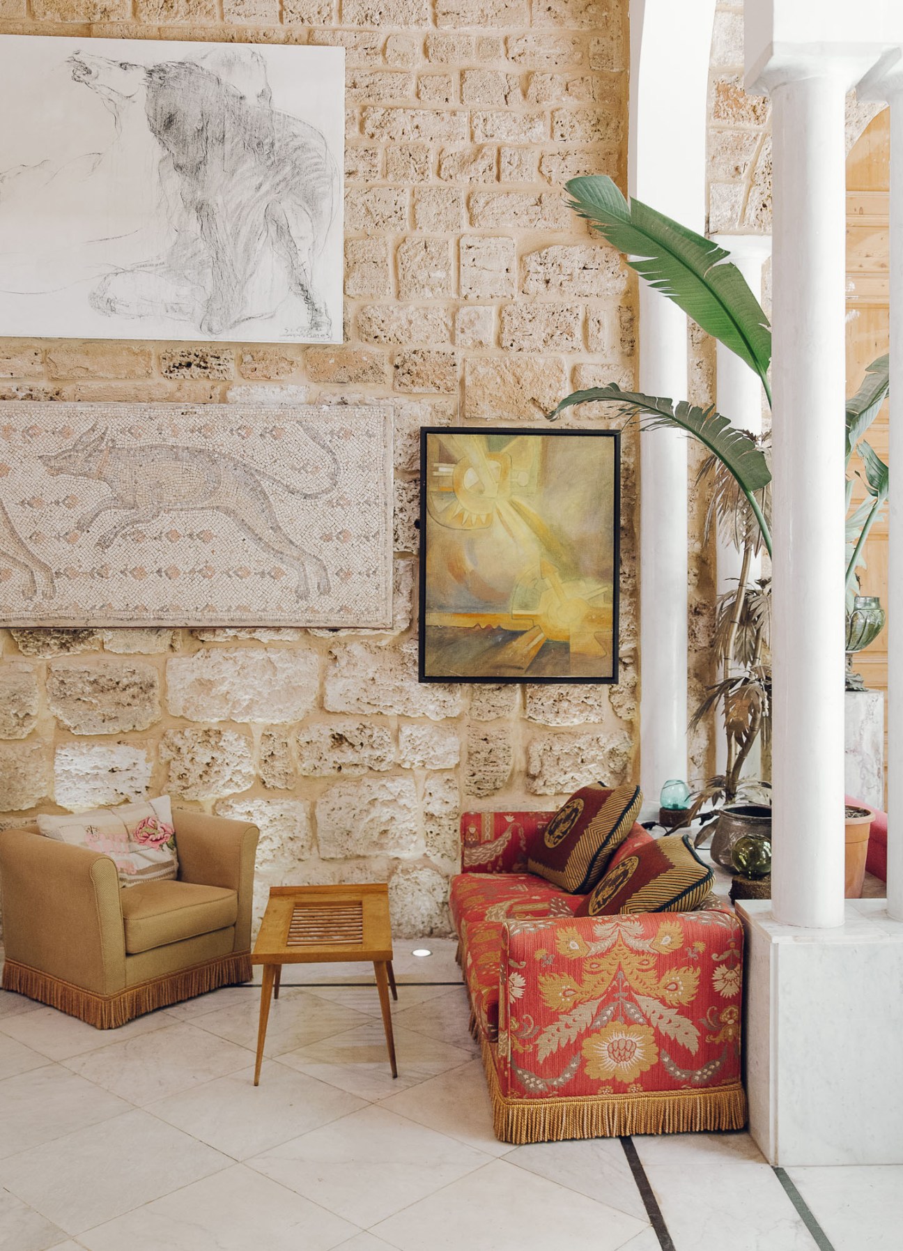Stone-walled lobby displaying contemporary artwork, vintage furniture, and potted plants.