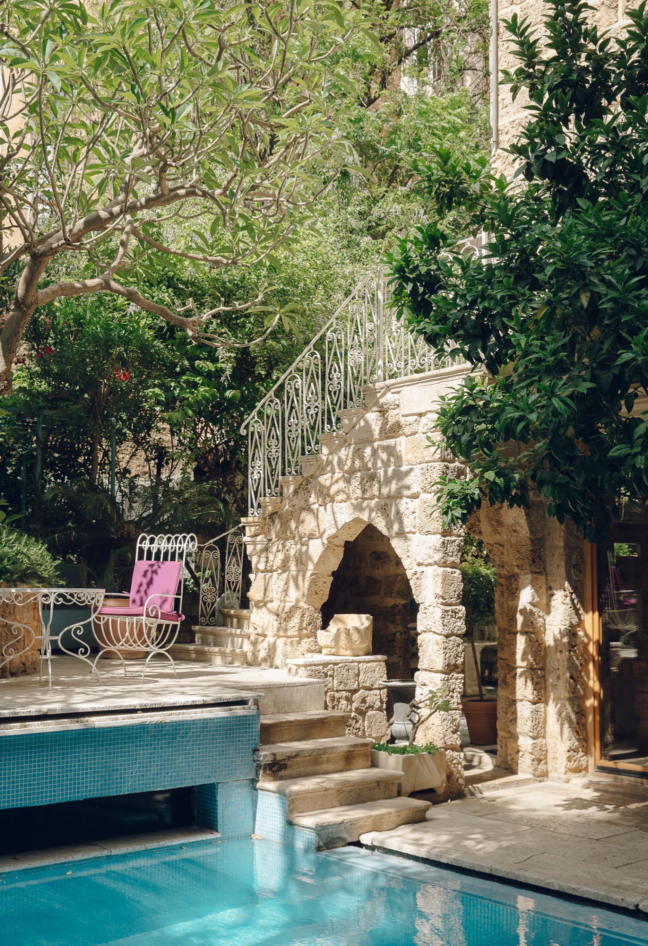 Arthaus hotel's pool and lush garden with stone architecture, ornate railings, and leafy trees.