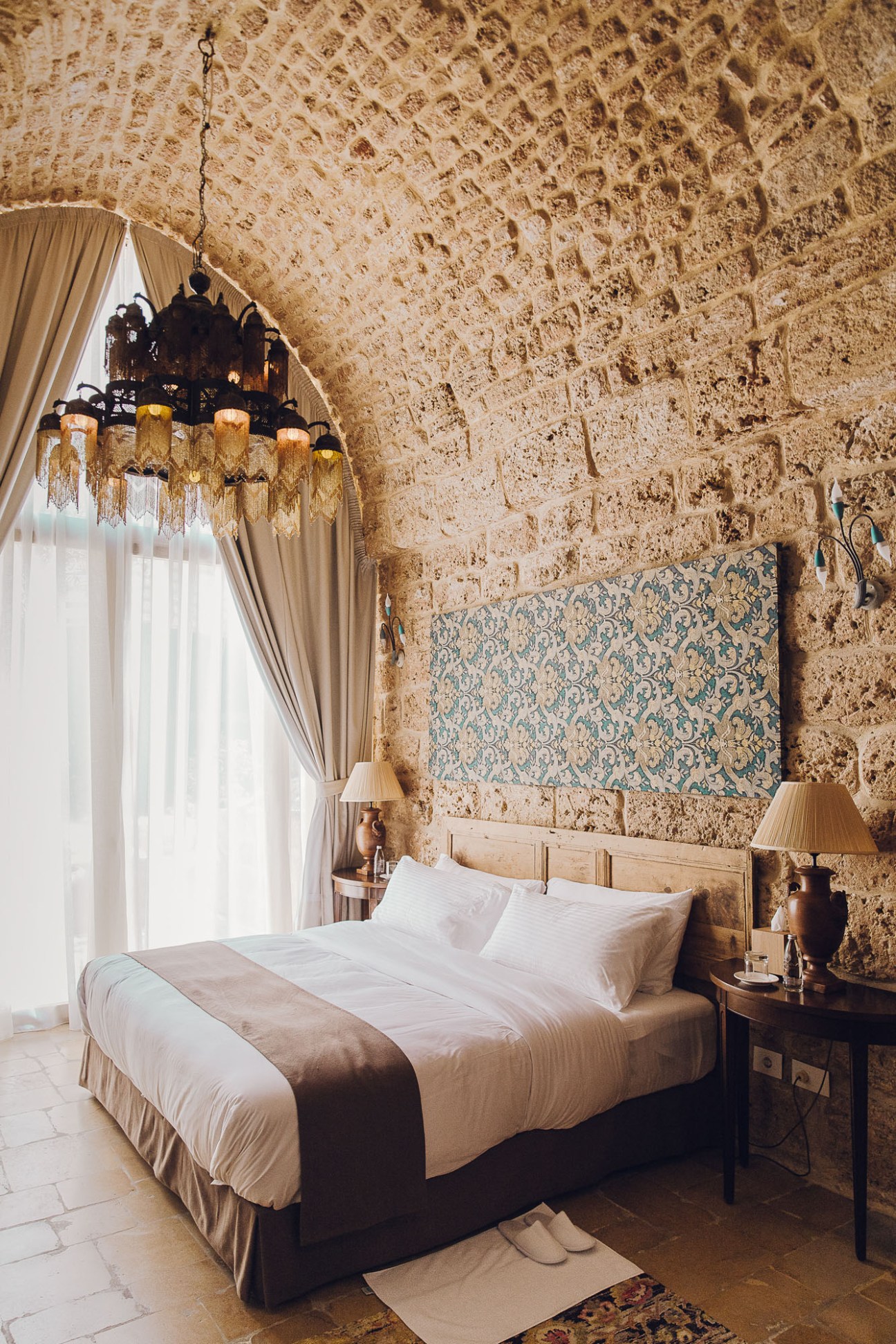 Hanna's Suite bedroom with exposed stone walls, ornate ceiling chandelier, and traditional patterned textile art.