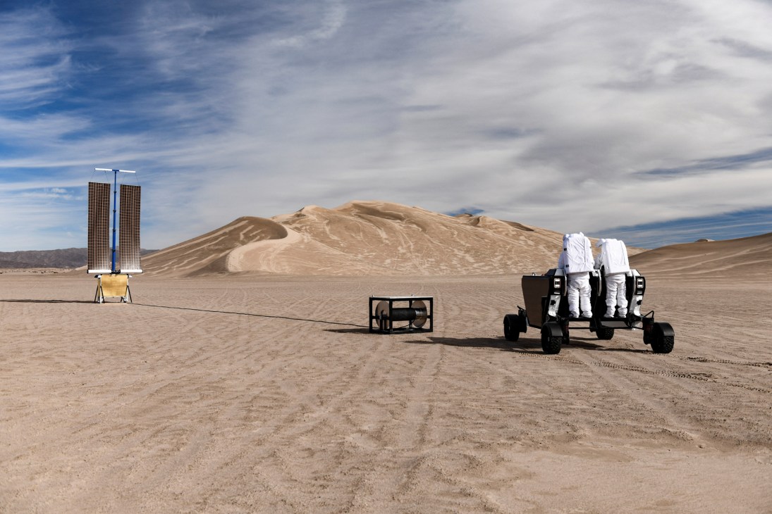 Two astronauts in white spacesuits testing Astrolab's Flex lunar rover prototype in desert terrain