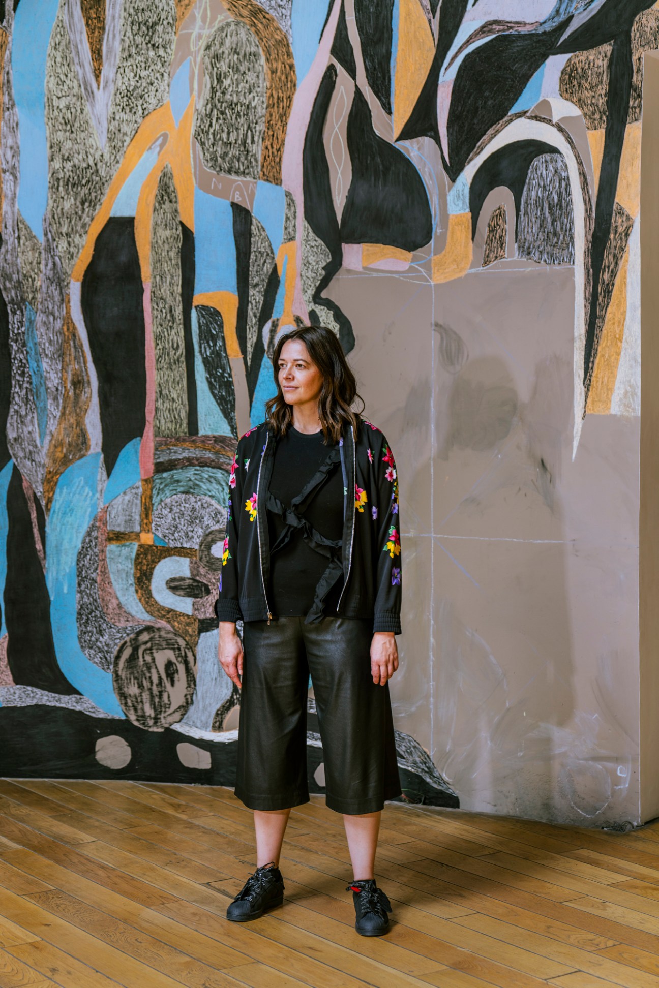 OMR partner Kerstin Erdmann stands in front of a large colorful mural artwork in the Lago gallery space
