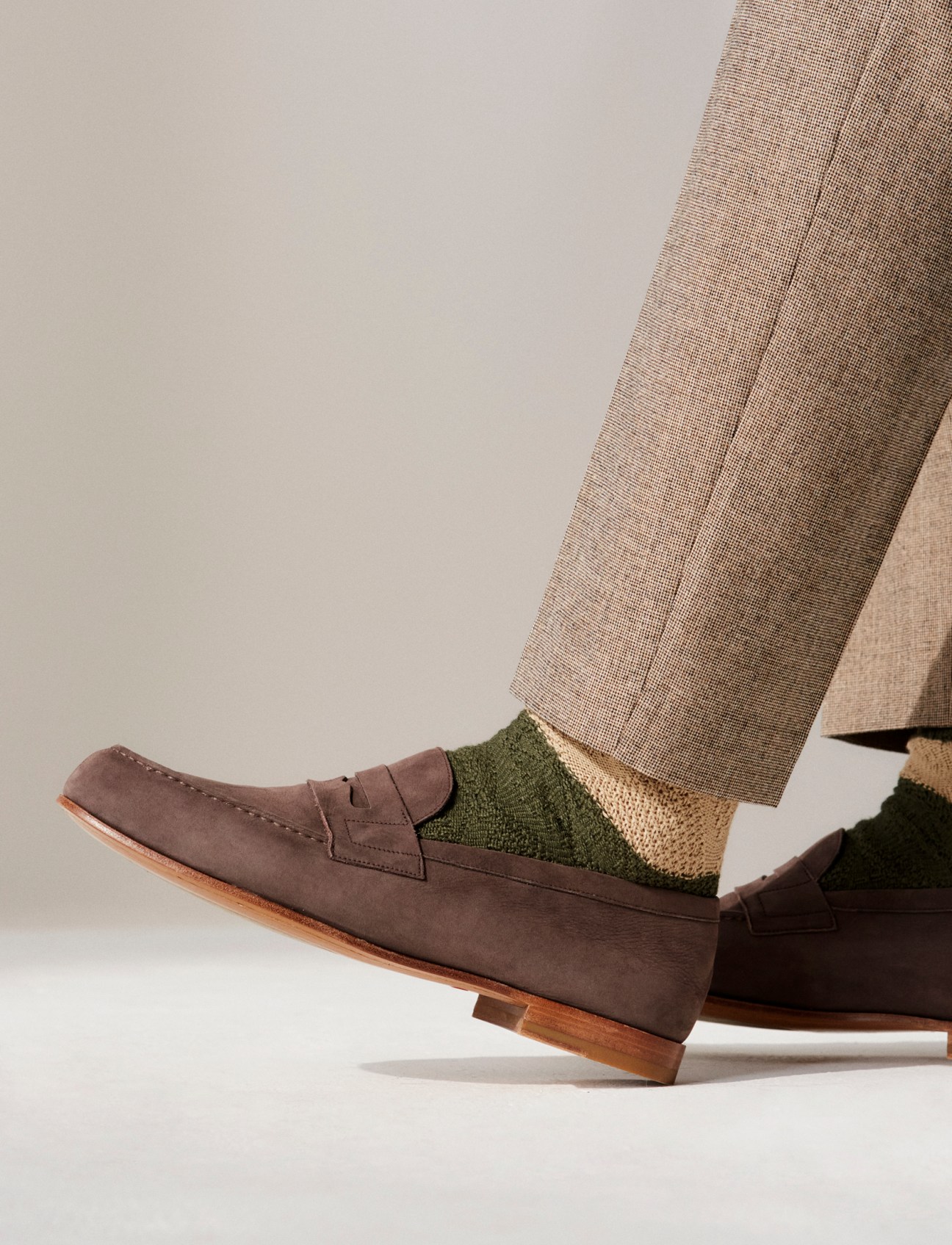 Detail shot of beige trousers, green and beige striped socks, and brown suede penny loafers