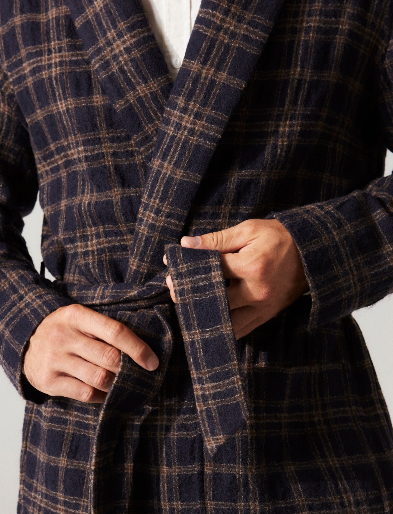 Model wearing navy checked robe or dressing gown with tie belt, hands adjusting the belt
