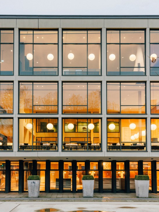 Paper lanterns glowing warmly through large windows of the Deutsche Oper building exterior at night