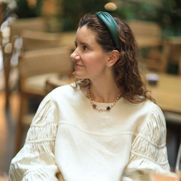 Woman in white ruffled top with green headband looking to the side in profile