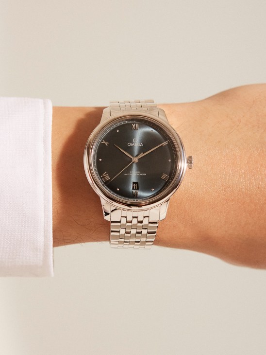 Person wearing an Omega De Ville Prestige watch with dark dial and steel bracelet on their wrist