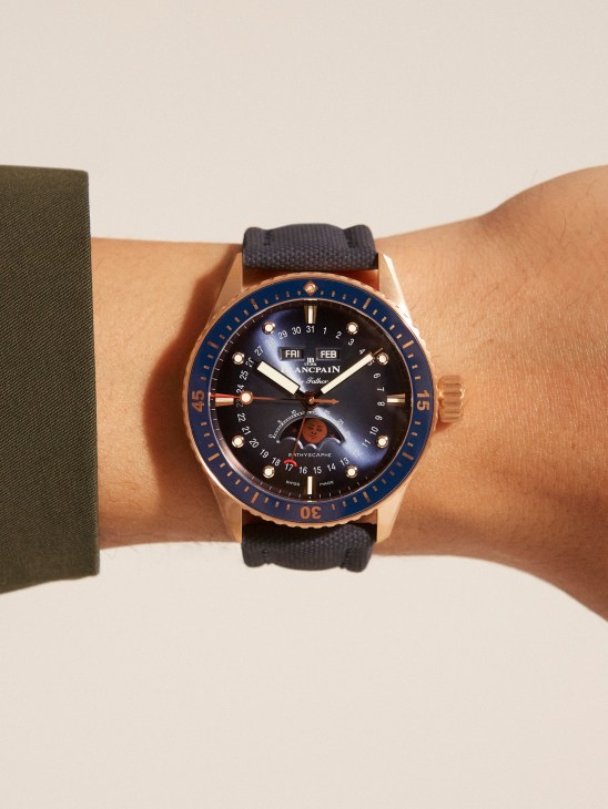 Blancpain Fifty Fathoms Bathyscaphe watch with rose gold case, blue bezel, and black canvas strap worn on wrist