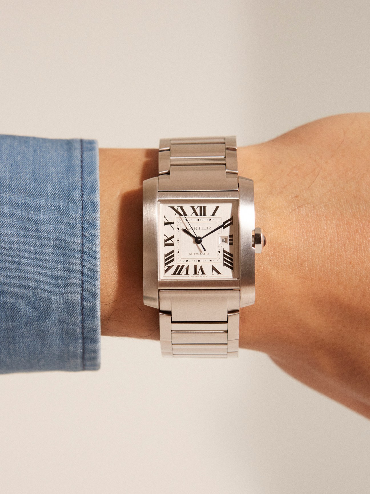 Cartier Tank Française watch with silver band and cream dial on wrist, worn with blue shirt sleeve.