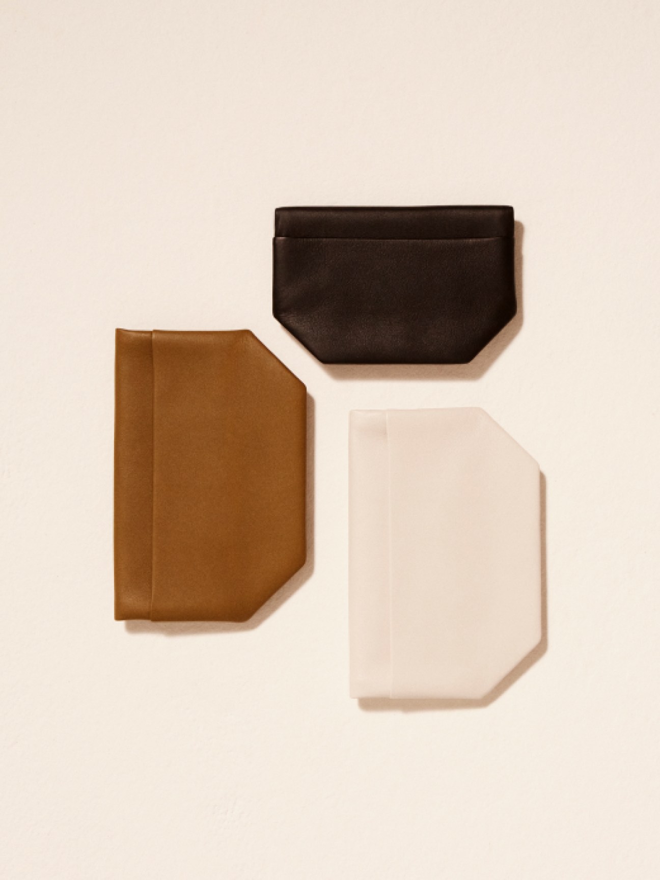 Three geometric leather pouches in brown, black, and cream colors arranged on neutral background