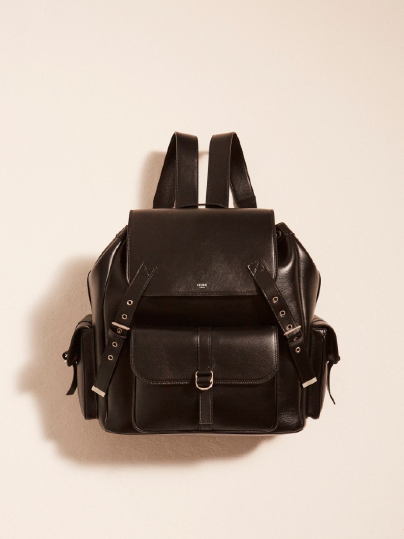 Black leather backpack with buckled front pocket and adjustable straps against cream background