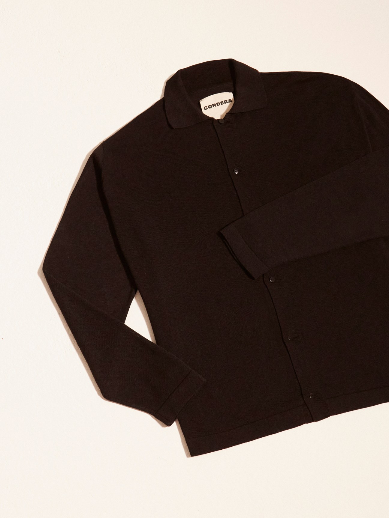Cordera black wool shirt jacket with collar and button front on cream background.