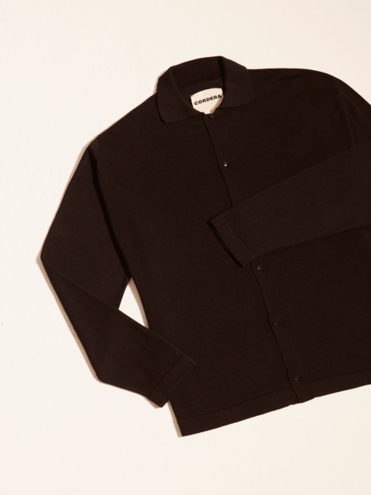 Black long-sleeved button-up shirt with CORDERA label laid flat on light background