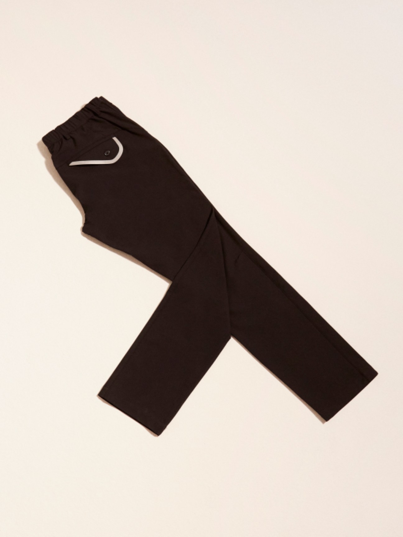 Black tailored trousers with white curved logo detail laid flat against beige background