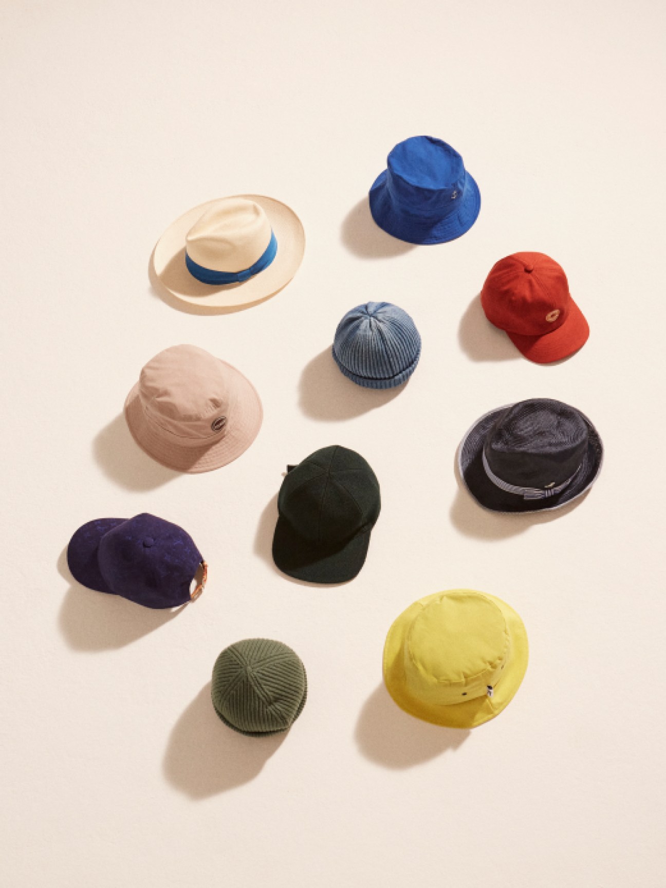 Collection of spring hats in various styles and materials arranged on neutral background