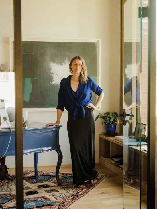 Woman in blue shirt standing in modern interior with artwork, plants, and wooden furniture