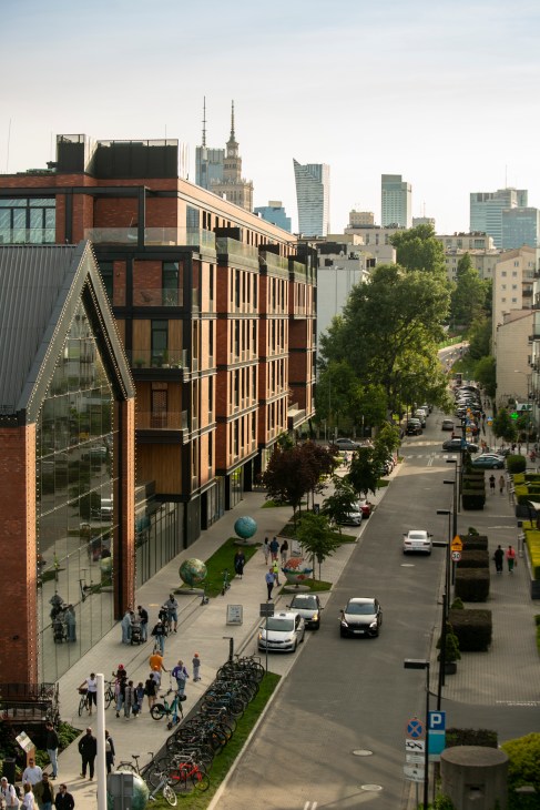 A street scene in Warsaw showing modern urban architecture with pedestrians walking along a busy sidewalk